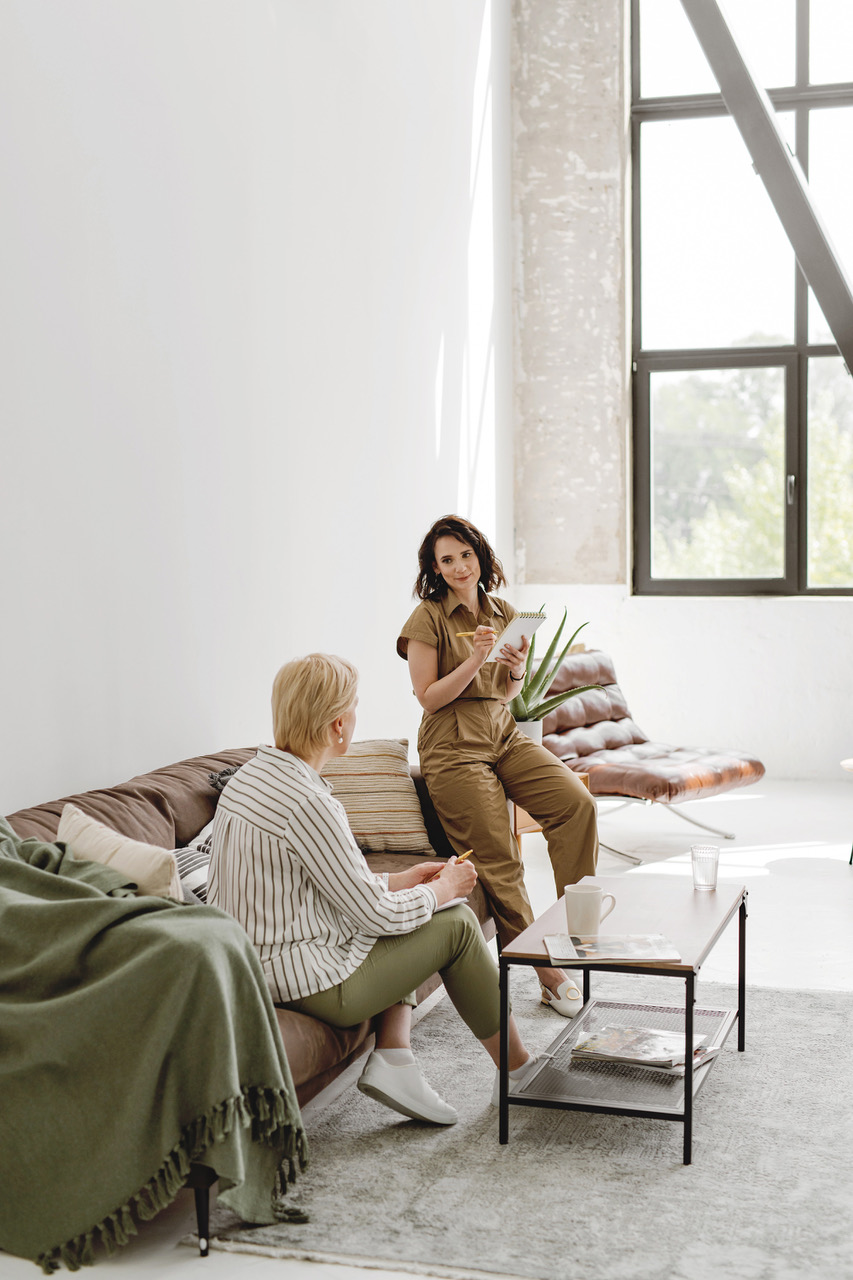 zwei Frauen in grünen Farben gehalten bei einem Coaching. Eine Frau sitzt auf einer Couch und die andere lehnt sich an die Lehne der Couch.