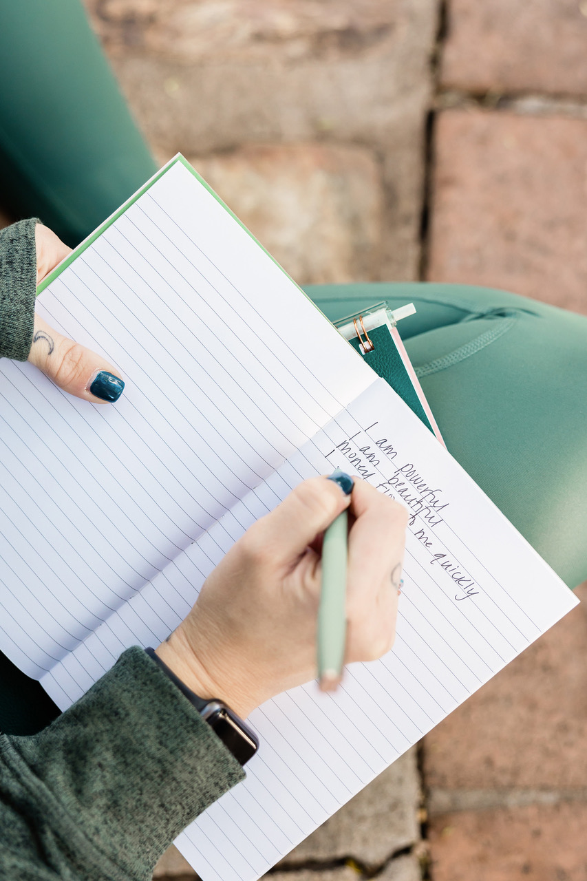 Frauenhand, die positive Gedanken und Affirmationen mit einem grünen Stift in ein Journal schreibt.