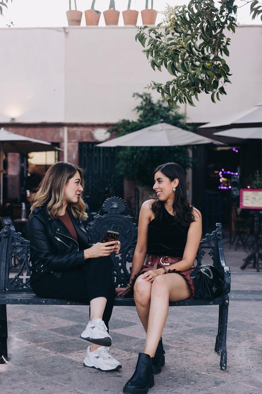 two girls sitting on a bench. One is talking and the other girl listens with intent. Communication with interest.